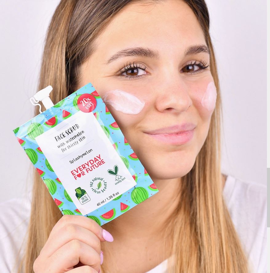 Ragazza sostiene in mano lo scrub viso di Everyday for Future al riso e anguria, sulle guance resta applicato lo scrub per far vedere la texture